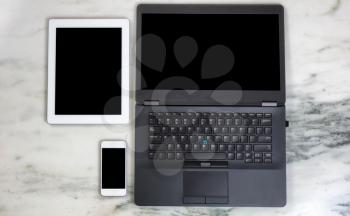 Overhead view of modern wireless mobile communication devices and computer on marble desktop. Paperless office concept.  