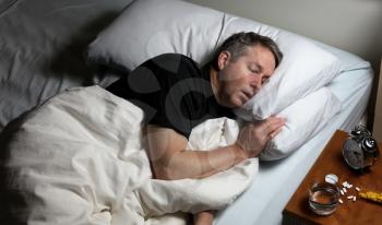 Mature man resting head in pillow while trying to sleep in bed. Insomnia concept with pain medicine on nightstand. 