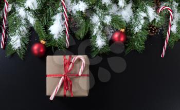 Christmas gift with snowy evergreen tree branches, candy canes and red ornaments on black background 