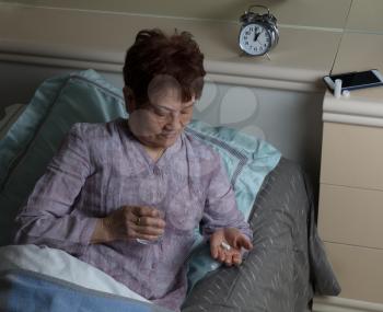senior woman taking medicine during nighttime while in bed