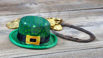 Lucky green hat, horseshoe and gold coins for St Patrick on rustic wooden boards in close up view 
