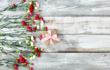 Colorful carnations and gift forming left border on white weathered wooden boards 