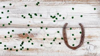 St Patrick day good luck horseshoe with shiny clovers on rustic white wooden boards in overhead view 