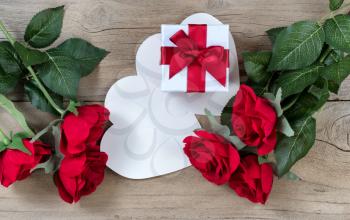 red roses surrounding white gift box on weathered wooden background in flat lay view 