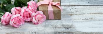 Front view of a half a dozen pink roses and gift box on rustic white wood in flat lay view