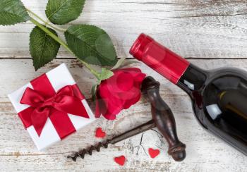 Valentines gift with red wine, rose and corkscrew opener on rustic white wood in overhead view