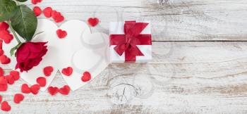 Valentines card with red heart shapes, gift and a single rose on rustic white wood in flat lay view