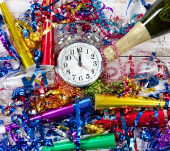 Happy New Year Celebration with clock striking twelve in center of party objects on white rustic wood 