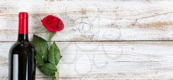 Romantic Valentines Day celebration with red wine and a single rose on white rustic wood 