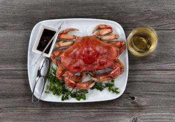 Whole Dungeness crab in dinner setting with wine on wooden table in top view layout