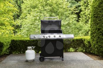 large barbeque cooker, with lid up, on concrete outdoor patio with woods in background
