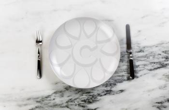 Dinner setting with clean plate, knife and fork on marble table  