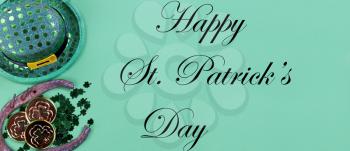 St Patricks day holiday celebration with Irish elf hat, horse shoe, gold and small clovers on a green paper background with copy space plus text message