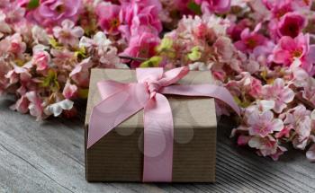 Close up of a gift box with pink cherry blossoms in background on weathered wooden planks for Mothers day love holiday concept 