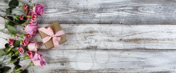 Real pink rose and carnation flowers with a giftbox on left side of rustic wooden planks for mothers day or valentines holiday 