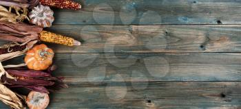 Aging pumpkins and corn on faded blue wood planks for either a Halloween or Thanksgiving holiday concept background 