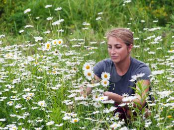beautiful young woman sitting on a flowering meadow with daisies