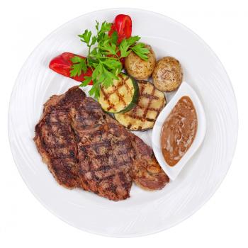 Grilled steaks, baked potatoes and vegetables on white plate isolated on white background.