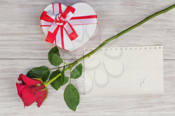 Valentine`s Day gift, rose and paper on wooden background. Closeup.