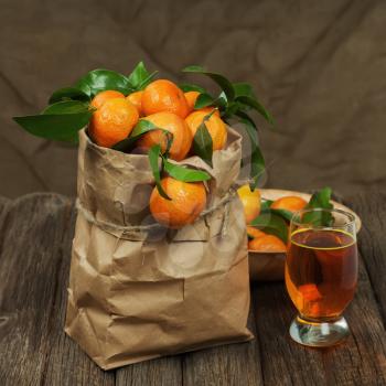 Fresh tangerines in recycle paper bag and glass of juice on wooden table. Closeup.