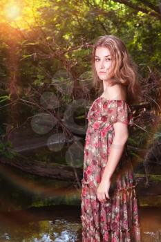 Beautiful girl in floral dress in forest. Soft sunny colors.