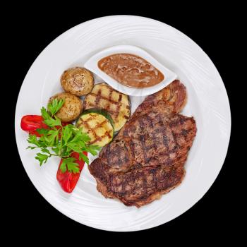 Grilled steak, baked potatoes and vegetables on white plate on black background.