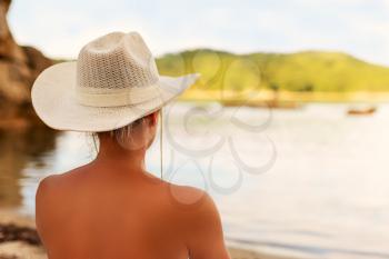 Young woman in a white hat is looking on beautiful beach and islands. Photo is in soft sunny colors.