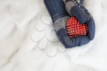 Woman hands in light teal knitted mittens are holding red heart on snow background. Winter, Valentines and Christmas concept.