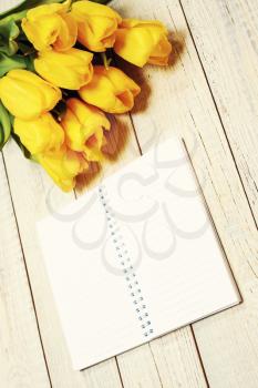 Fresh yellow tulips with empty open notepad on wooden background.  Top view with copy space. Photo with retro filter effect.