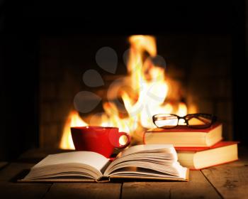 Red cup of coffee or tea, glasses and old books on wooden table near fireplace. Winter and Christmas holiday concept.