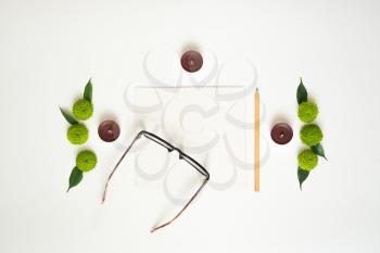 Paper, pencil, glasses and candles with decoration of chrysanthemum flowers and ficus leaves on white background. Overhead view. Flat lay.