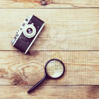 Vintage, very old film camera and magnifying glass on brown wooden background and space for text. Photo with retro filter effect.
