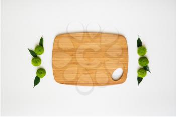Wooden cutting board with decoration of chrysanthemum flowers and ficus leaves on white background. Overhead view. Flat lay.