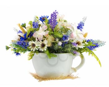 Table floral arrangement made of artificial flowers and cottons balls in stylized ceramic vase in form of tea cup isolated on white background.