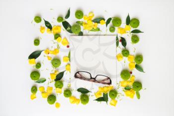 Glasses and paper with pattern from petals of roses and chrysanthemum flowers, ficus leaves and ripe rowan on white background. Overhead view. Flat lay.