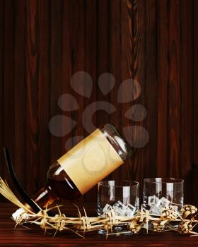 Two glasses with ice for whiskey and bottle on dark wooden background.