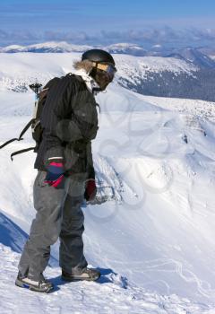 The snowboarder-freerider is standing on the brink of a precipice and looking down.