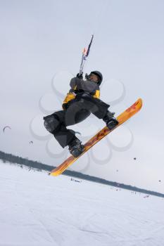 The snowkiter on the orange snowboard is jumping over the camera.