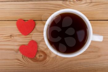 Cup of coffee and two hearts on a wooden background.