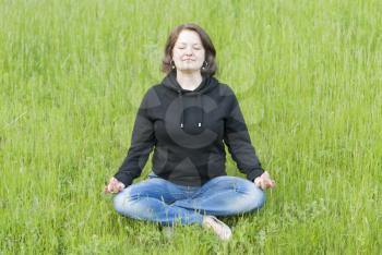Woman meditating in the lotus position on the green grass in the park.