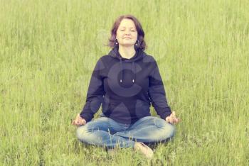 Woman meditating in the lotus position on the green grass in the park.