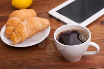 Cup of coffee and a croissant on the table tablet.