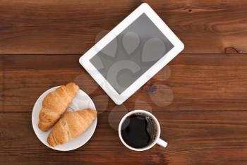 Coffee digital tablet and croissants on a wooden table.