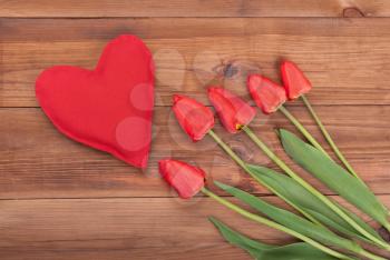 Red tulips and heart on a wooden background. View from above .