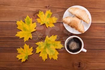 Coffee, croissants and maple leaves on wooden background.
