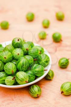 White Dish Filled With Succulent Juicy Fresh Ripe Green Gooseberries On An Old Wooden Table Top.