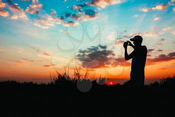 Silhouette Of Young Man Photographing The Sunset On Smartphone Or Camera On Background Of Colourful Evening Sky