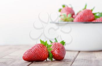 two strawberries closeup on the foreground on the background of a full bowl of strawberries