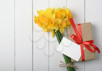 daffodils with a gift box and a note on a white wooden background