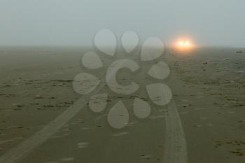 Car headlights of a car on the beach, mist